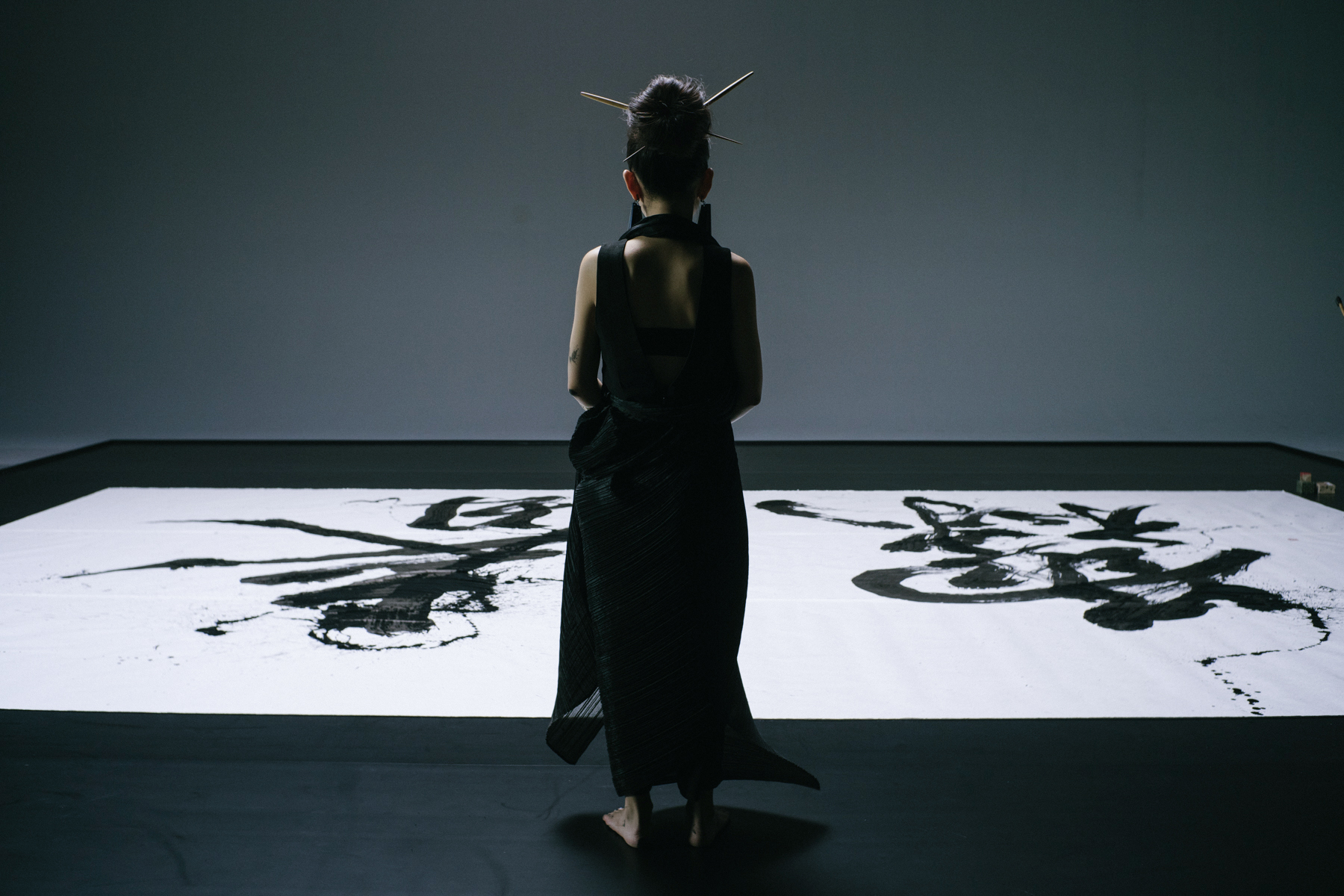 image sur les tons bleu terne foncé, avec Aoi Yamaguchi debout devant une des ses œuvres.